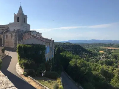 a building on a hill with a tower in the distance at Mas Saint-Genies in Venasque