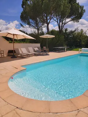 a swimming pool with two umbrellas and a table and chairs at Gîte élégant au calme in Mazan
