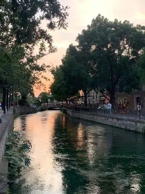 a river in a city with people walking on a bridge at La terrasse du pont jullian charme et calme dans le cœur historique in LʼIsle-sur-la-Sorgue