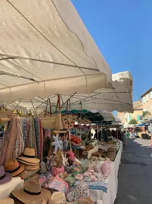 a market with hats and hats on display under a large umbrella at La terrasse du pont jullian charme et calme dans le cœur historique in LʼIsle-sur-la-Sorgue
