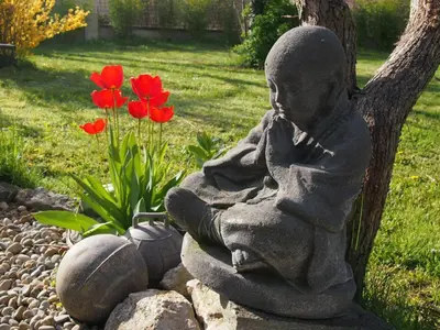 a statue of a little girl sitting in a garden with red flowers at L'Islo Bamboo in Saumane-de-Vaucluse