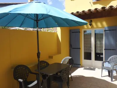a table and chairs with a blue umbrella on a patio at vacances en provence cyprès in Mormoiron