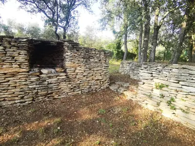 an old stone wall with trees in the background at Le Fiacre entre chênes et oliviers dans le Luberon in Cabrières-dʼAvignon