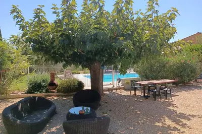 a tree with chairs and a table next to a pool at Le Cavaou in Mérindol