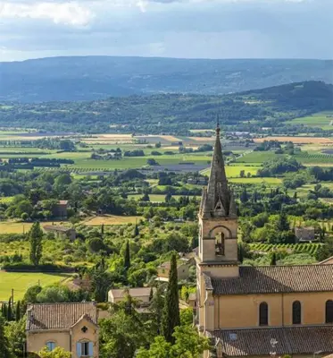 a church with a steeple in the middle of a field at BOHO 2 Vue Panoramique in Bonnieux
