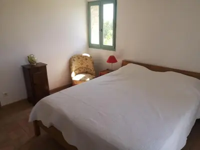a bedroom with a bed and a chair and a window at Les Vendangeurs, gîte au milieu des vignes face au Luberon in Goult