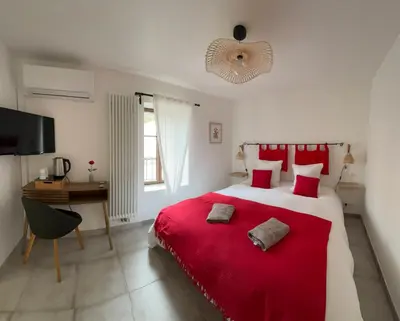 a bedroom with a large bed with red sheets and a desk at L’auberge de Montsalier in Montsalier