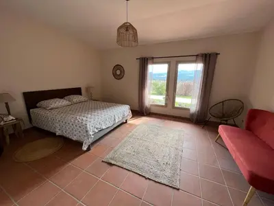 a bedroom with a bed and a couch and a window at Proche Roussillon, La villa rouge Luberon, piscine chauffée, climatisation et vue Luberon in Gargas