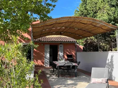 a patio with a table and chairs under a wooden umbrella at Proche Roussillon, La villa rouge Luberon, piscine chauffée, climatisation et vue Luberon in Gargas