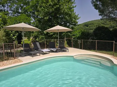 a swimming pool with two chairs and umbrellas at Mas Cerisiers in Saint-Martin-de-Castillon