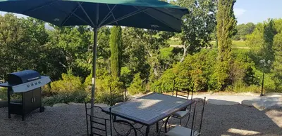 a table with an umbrella next to a grill at Gîtes L'HERMITAGE in La Tour-dʼAigues