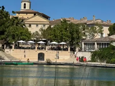 a building with tables and umbrellas next to a body of water at LES CISTES in Mallemort