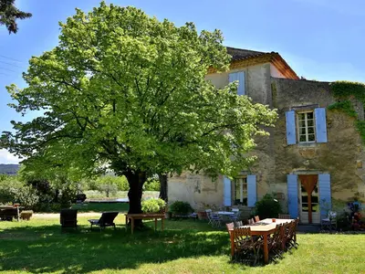 a tree in front of a house with a table and chairs at Domaine la Carraire in Lauris