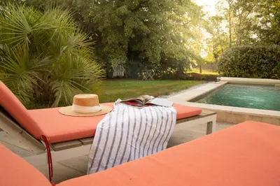a hat and a towel sitting on a table next to a pool at Maison Loutina, Villa 5 min à pied du centre in LʼIsle-sur-la-Sorgue