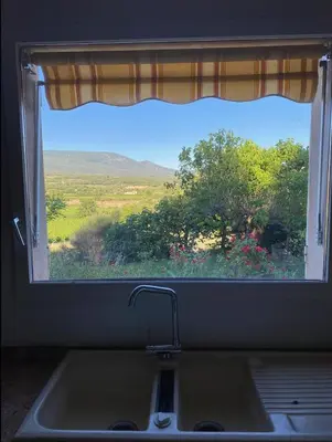 a window over a kitchen sink with a view of a field at Jolie maison avec vue imprenable, piscine, jeu de boules, calme au cœur du Luberon in Les Cordiers
