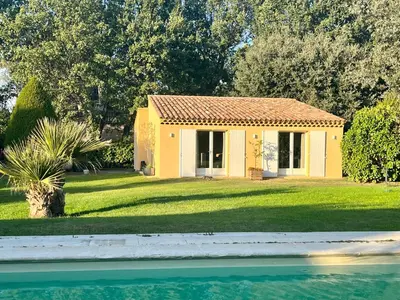 a small yellow house in a yard next to a body of water at Charmante maisonnette avec jardin et piscine in Aix-en-Provence