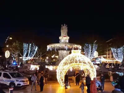 a group of people walking around a christmas market at night at Aix en Provence - Rotonde - Cours Mirabeau in Aix-en-Provence