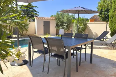 a dining table and chairs with an umbrella on a patio at Les Lauriers Blancs air-conditioned villa with swimming pool in LʼIsle-sur-la-Sorgue