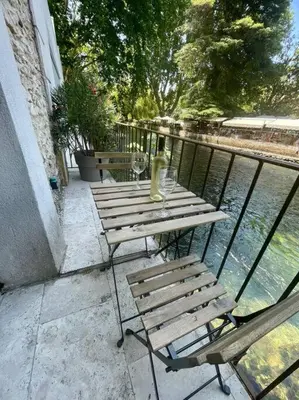 a table and chairs sitting on a balcony next to the water at Jacuzzi & Terrasse en bord de rivière in Fontaine-de-Vaucluse