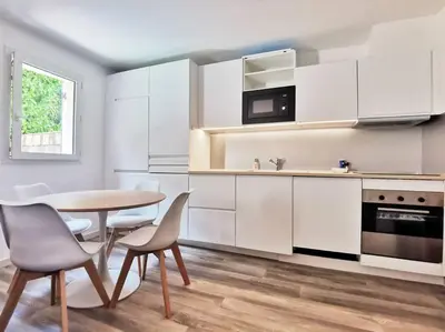 a kitchen with white cabinets and a table and chairs at Les quatre loges - joli t2 jardinet et parking *3 in Aix-en-Provence