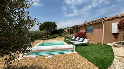 a backyard with a swimming pool with two white chairs and a house at La Villa Tanamera, très jolie maison piscine, à 2 pas du centre-ville in Bédoin