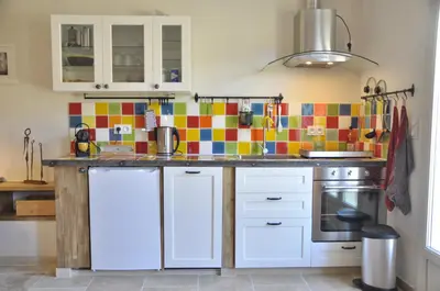 a kitchen with white cabinets and a colorful tile wall at Gite Hardy in Velleron