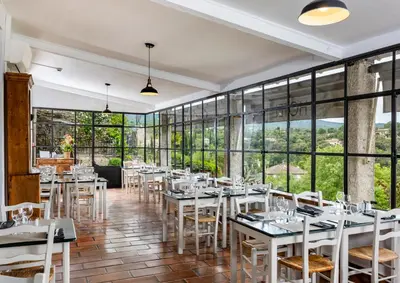 a restaurant with white tables and chairs and large windows at Hôtel Restaurant Les Remparts in Venasque