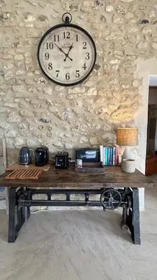 a clock hanging on a stone wall above a bench at La Bergerie des Pottiers. Mas rénové climatisation Piscine in Crillon-le-Brave