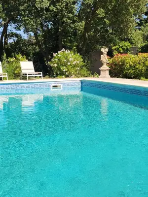 a blue swimming pool with two chairs and a fountain at Le Clos Renaissance in Oppède