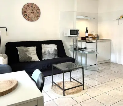 a living room with a black couch and a clock at Studio cœur de ville avec salle de bain privative & kitchenette in Carpentras