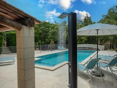 a pool with a fountain and two chairs and an umbrella at La Cadeline in Saumane-de-Vaucluse