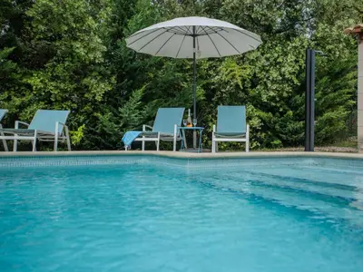 a pool with chairs and an umbrella and a table at La Cadeline in Saumane-de-Vaucluse