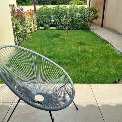 a metal bench sitting on a sidewalk next to a yard at Gîte Le Jasmin in Le Thor