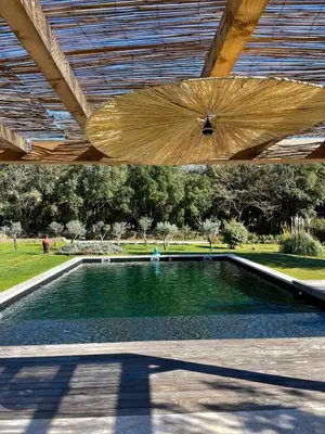 a swimming pool under a wooden roof with an umbrella at Domaine d'Hestia le gite Victoria in Rognes