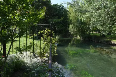 a river with trees and a fence next to it at Profitez de la quiétude en bord de rivière, à 5 min du centre ville in LʼIsle-sur-la-Sorgue