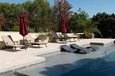 a swimming pool with chairs and umbrellas next to a swimming pool at Gîte Thaliana in Saumane-de-Vaucluse