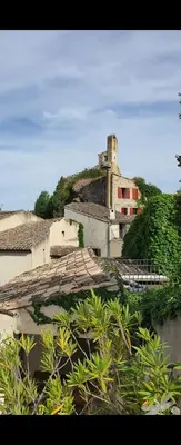 a building with a tower on a hill with trees at Clos des Jasmins avec sa jolie cour intérieure in Lourmarin