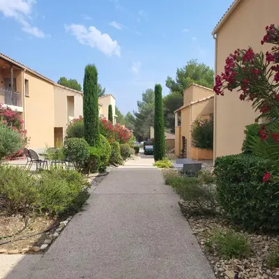 a walkway between two buildings with cypress trees at La Calade in LʼIsle-sur-la-Sorgue