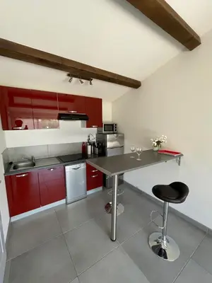 a kitchen with red cabinets and a table with a stool at Studio charmant avec terrasse in Lançon-Provence