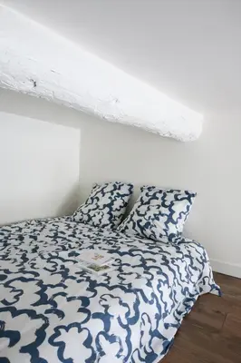 a bed with a blue and white comforter and a pillow at Cocon provençal dans le centre historique in Aix-en-Provence