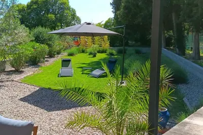 a garden with an umbrella and chairs and grass at Gîte cosy au coeur du Luberon in Lagnes
