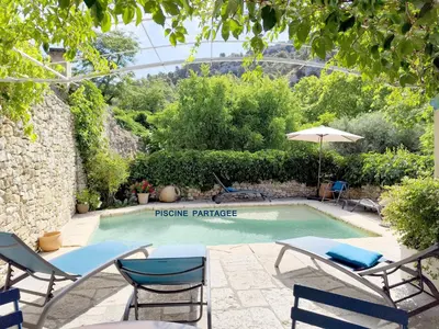a swimming pool in a garden with chairs and an umbrella at Les trois gites in Robion en Luberon