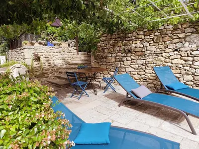 a patio with chairs and a table and a stone wall at Les trois gites in Robion en Luberon