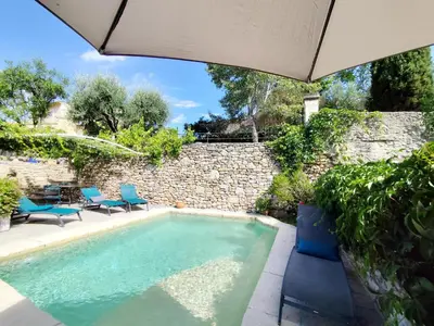 a swimming pool with two chairs and an umbrella at Les trois gites in Robion en Luberon