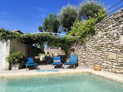 a swimming pool with two blue chairs and a stone wall at Les trois gites in Robion en Luberon