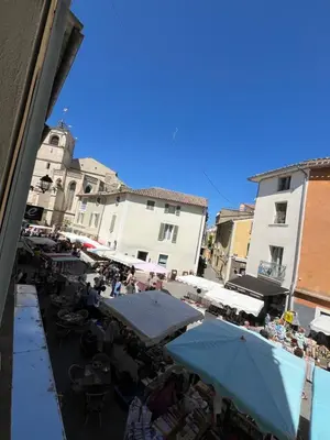 an outdoor market with tables and umbrellas and buildings at Logement studio avec vue sur le centre Historique in LʼIsle-sur-la-Sorgue