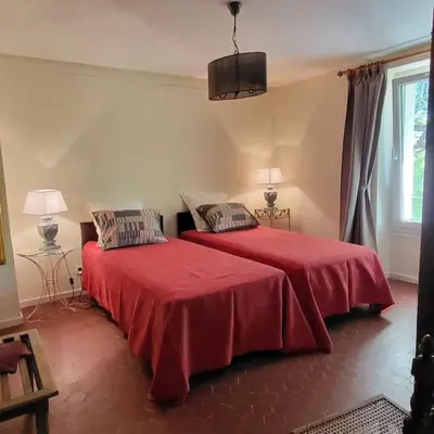 a bedroom with two beds with red sheets and a window at L' Escale in Bonnieux