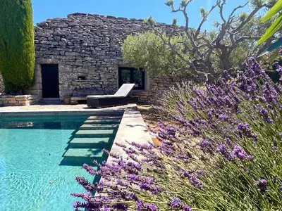 a pool with a bench next to a stone building at Le Clos de Yann in Gordes