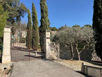 an iron gate with a stone wall and trees at Mas la Floreline in Cheval-Blanc