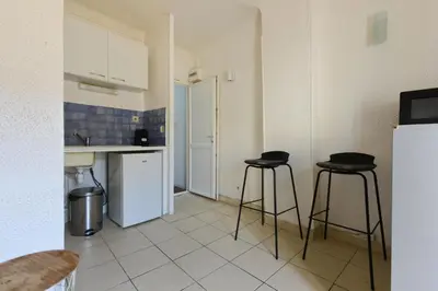 a kitchen with two bar stools and a white refrigerator at Studio Lavande in La Fare-les-Oliviers